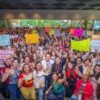 Multitud de mujeres de distintas edades y vestimentas reunidas en una asamblea al aire libre en Morelia, con pancartas y banderas, escuchando a Carlos Torres Piña.