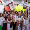 Carlos Torres Piña hablando ante una multitud en una asamblea regional en Pátzcuaro, Michoacán, con banderas purépechas visibles en el fondo