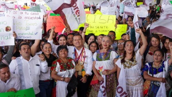 Carlos Torres Piña hablando ante una multitud en una asamblea regional en Pátzcuaro, Michoacán, con banderas purépechas visibles en el fondo