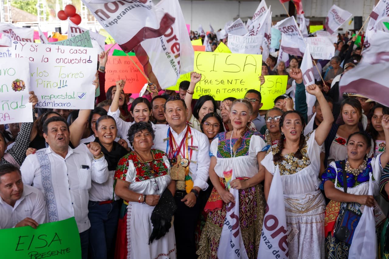 Carlos Torres Piña hablando ante una multitud en una asamblea regional en Pátzcuaro, Michoacán, con banderas purépechas visibles en el fondo