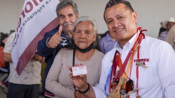 Carlos Torres Piña hablando ante un grupo de adultos mayores en Morelia, con bandera de México y logo de Pensiones del Bienestar visible