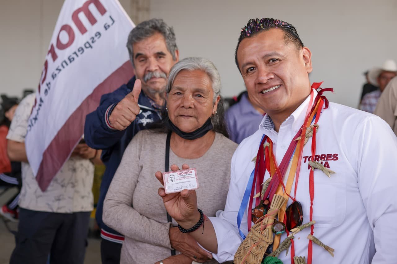 Carlos Torres Piña hablando ante un grupo de adultos mayores en Morelia, con bandera de México y logo de Pensiones del Bienestar visible
