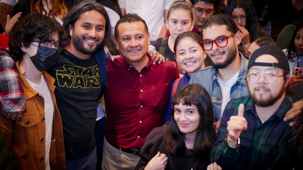 Retrato serio y accesible de Carlos Torres Piña en entorno comunitario, con fondo difuminado de vecinos conversando y carteles electorales discretos