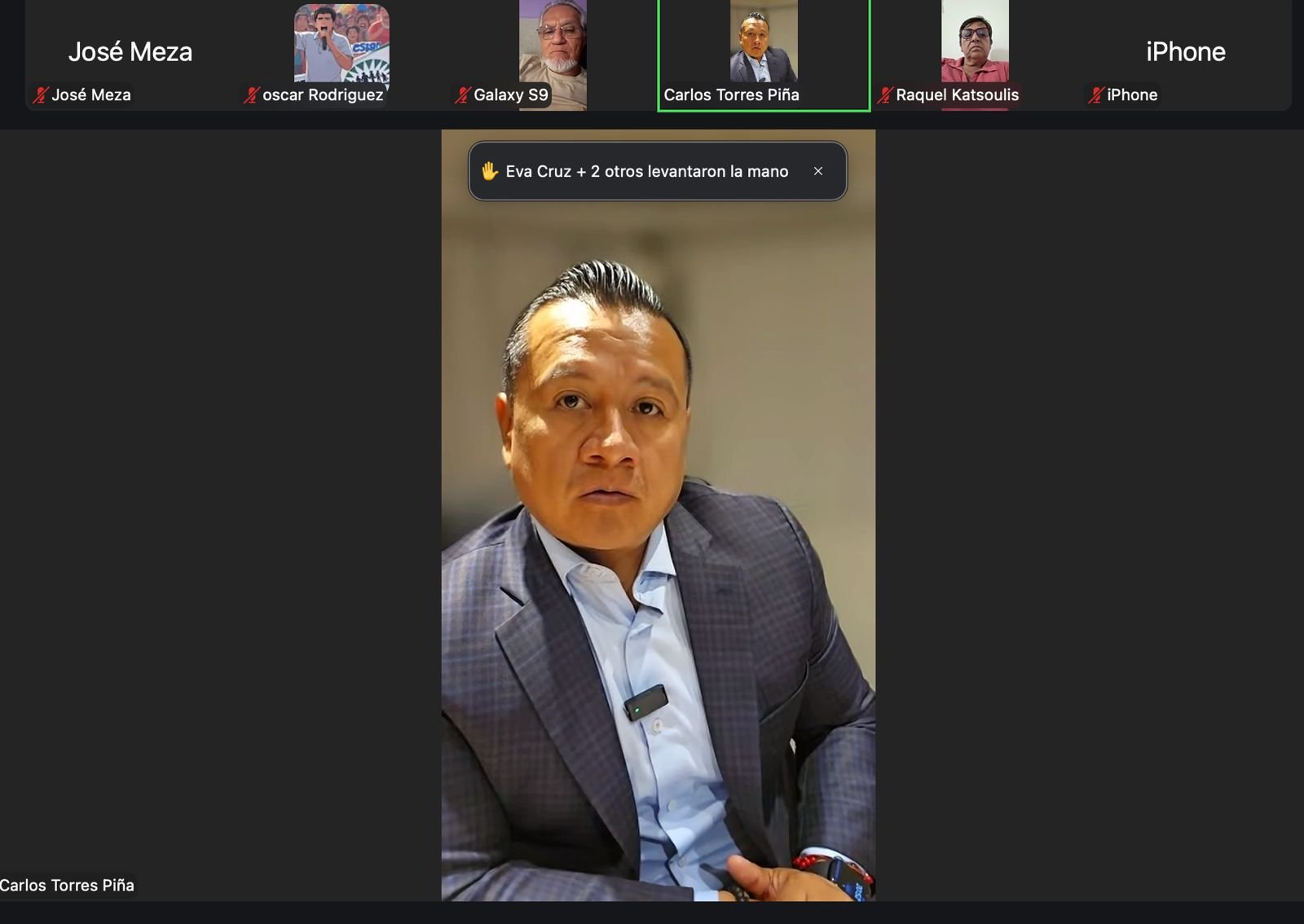 Carlos Torres Piña hablando frente a un mural con símbolos de Michoacán y una bandera mexicana, rodeado de migrantes y representantes comunitarios