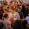 Carlos Torres Piña dialogando con ciudadanos en una comunidad rural de Michoacán, con fondo de bandera nacional y letrero del Plan Michoacán