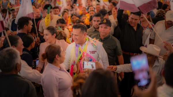 Carlos Torres Piña dialogando con ciudadanos en una comunidad rural de Michoacán, con fondo de bandera nacional y letrero del Plan Michoacán