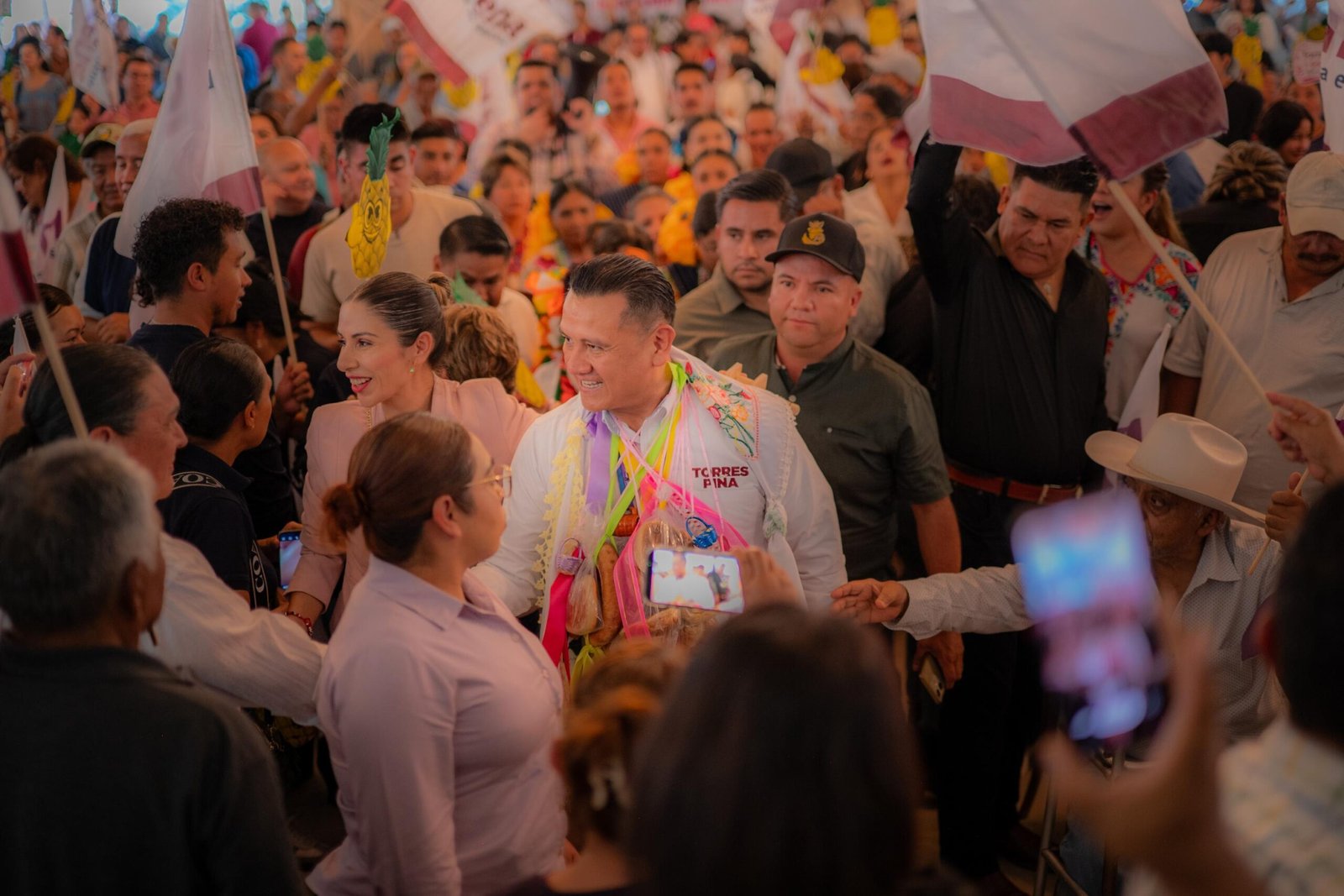 Carlos Torres Piña dialogando con ciudadanos en una comunidad rural de Michoacán, con fondo de bandera nacional y letrero del Plan Michoacán