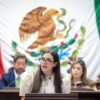 Diputada Giulianna Bugarini hablando ante micrófonos en el Congreso de Michoacán, con fondo del escudo estatal