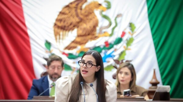 Diputada Giulianna Bugarini hablando ante micrófonos en el Congreso de Michoacán, con fondo del escudo estatal