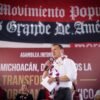 Carlos Torres Piña dialogando con ciudadanos de distintos sectores en un municipio rural de Michoacán, bajo un cielo despejado y con letreros comunitarios visibles