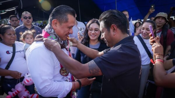 Fotografía de Carlos Torres Piña conversando con ciudadanos en un espacio público, con micrófono y libreta, durante uno de sus recorridos por el estado