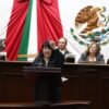 Ilustración simbólica de una mano extendiendo una bandera de Michoacán hacia un globo terráqueo, con siluetas de personas conectadas entre México y Estados Unidos