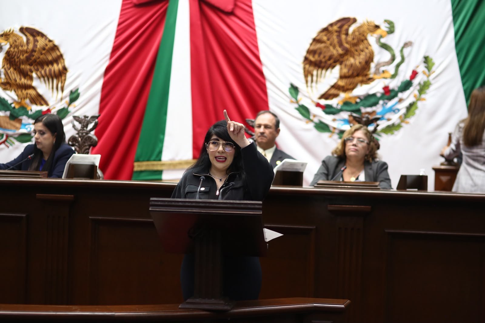 Ilustración simbólica de una mano extendiendo una bandera de Michoacán hacia un globo terráqueo, con siluetas de personas conectadas entre México y Estados Unidos