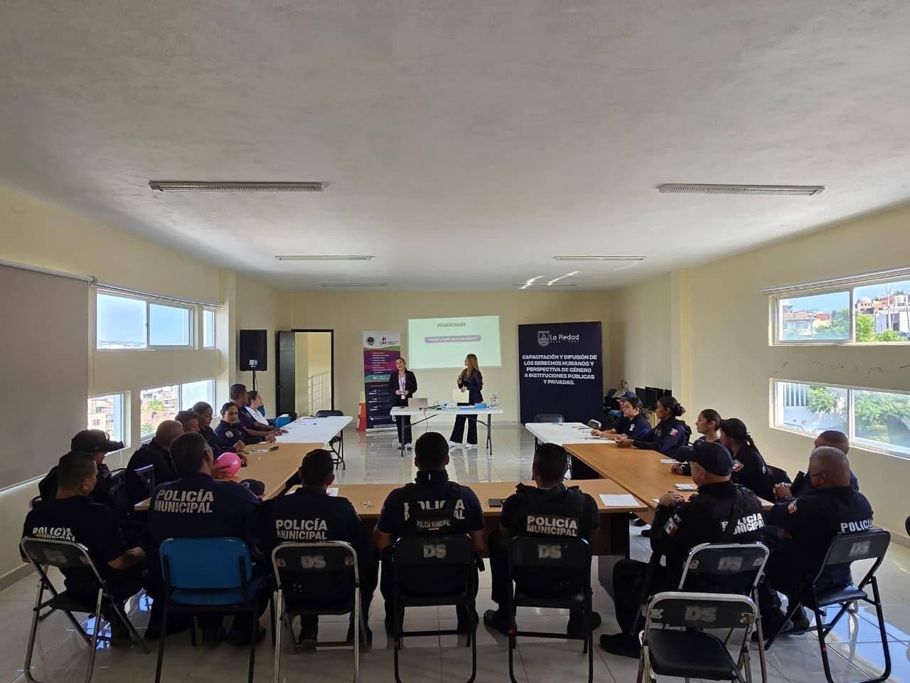 Grupo diverso de policías y personal administrativo de La Piedad participando activamente en un taller sobre apoyo a mujeres víctimas de violencia, con material educativo visible