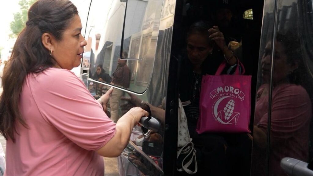 Fotografía de un autobús con logotipo de la Casa de Enlace Legislativo estacionado frente a un centro de salud en Morelia, con personas esperando su turno.