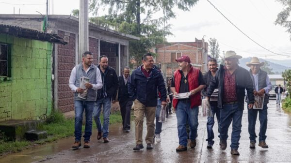 Fotografía de Carlos Torres Piña conversando con habitantes de un municipio michoacano, en entorno rural, con mapa de Michoacán visible de fondo