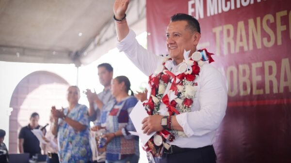 Carlos Torres Piña hablando ante vecinos de Tiripetío en la plaza principal, con bandera de Morena visible y público diverso de todas las edades