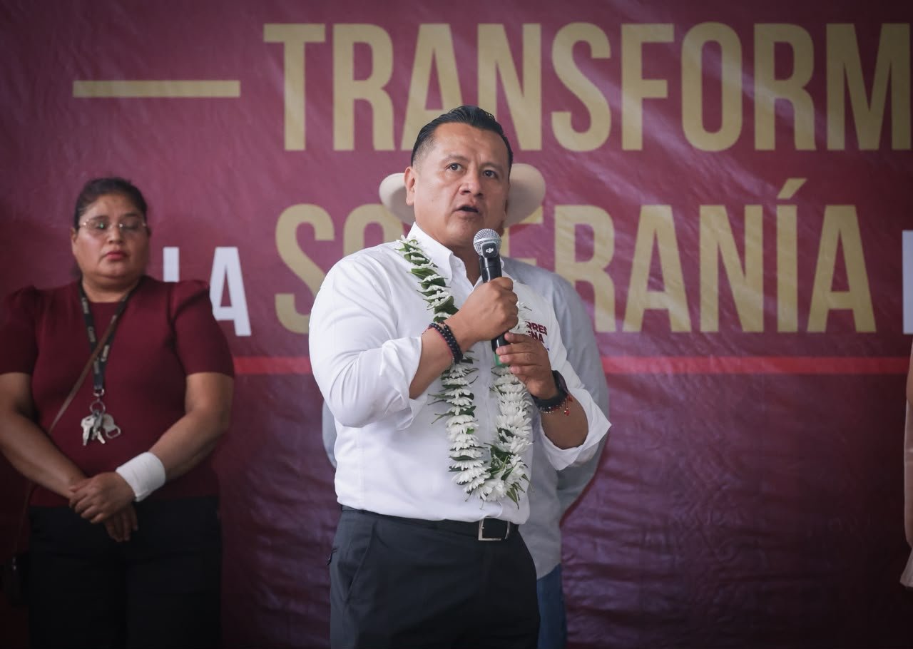 Carlos Torres Piña hablando frente a un micrófono con fondo de bandera mexicana, destacando seguridad y protección ciudadana