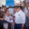 Carlos Torres Piña sentado en una reunión comunitaria, escuchando atentamente a un grupo diverso de ciudadanos en un espacio abierto de Michoacán