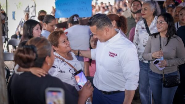 Carlos Torres Piña sentado en una reunión comunitaria, escuchando atentamente a un grupo diverso de ciudadanos en un espacio abierto de Michoacán