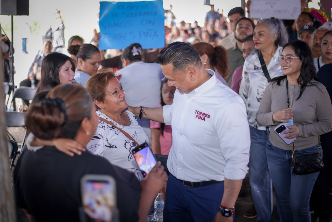 Carlos Torres Piña sentado en una reunión comunitaria, escuchando atentamente a un grupo diverso de ciudadanos en un espacio abierto de Michoacán