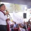 Carlos Torres Piña hablando ante micrófonos y bandera nacional en evento público en Morelia, Michoacán
