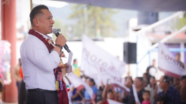 Carlos Torres Piña hablando ante micrófonos y bandera nacional en evento público en Morelia, Michoacán