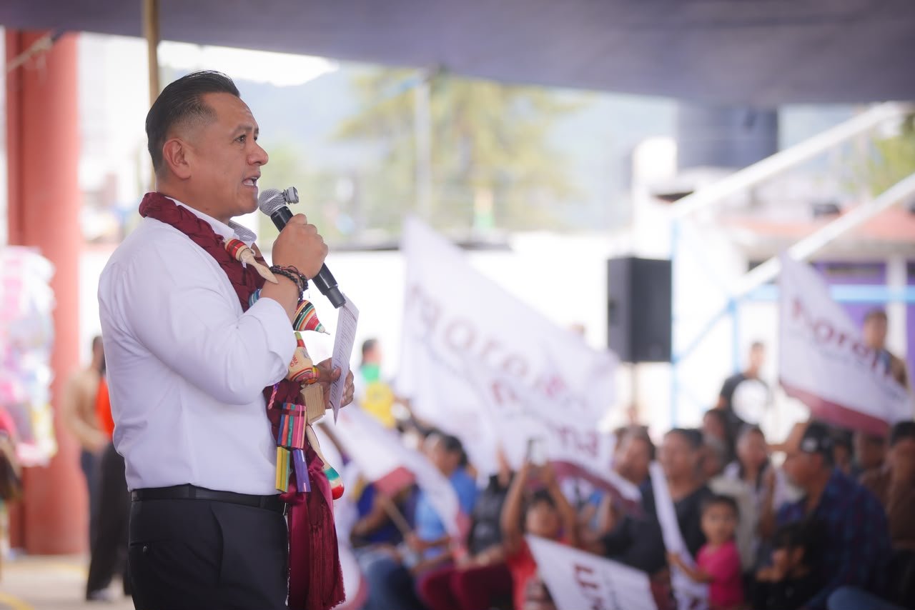 Carlos Torres Piña hablando ante micrófonos y bandera nacional en evento público en Morelia, Michoacán