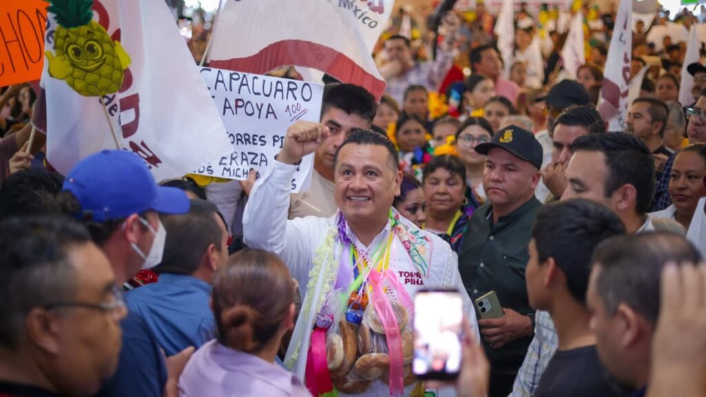 Fotografía de Carlos Torres Piña en una asamblea comunitaria al aire libre en Michoacán, escuchando a ciudadanos sentados en bancas de madera.
