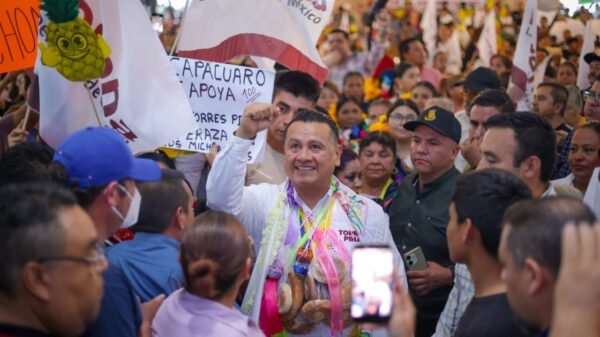 Fotografía de Carlos Torres Piña en una asamblea comunitaria al aire libre en Michoacán, escuchando a ciudadanos sentados en bancas de madera.