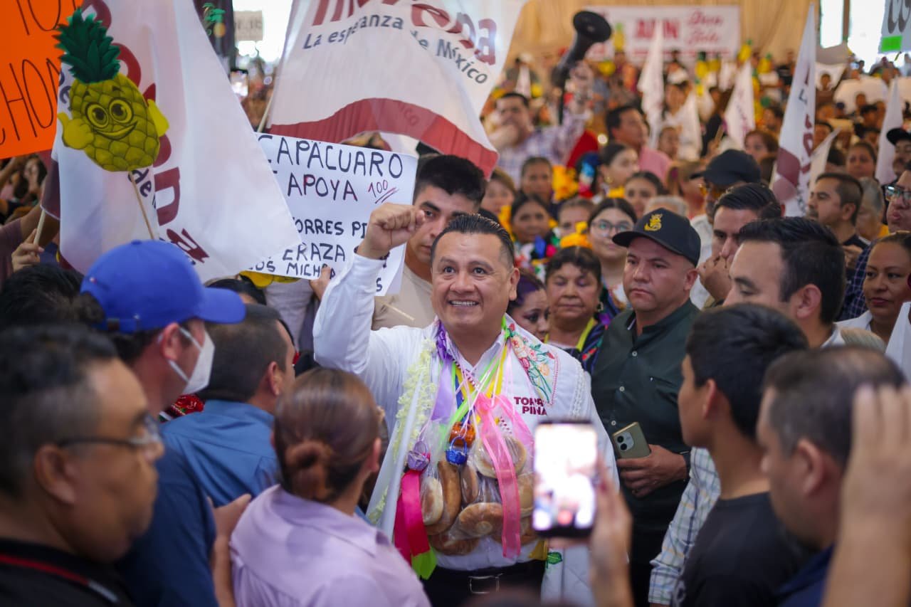 Fotografía de Carlos Torres Piña en una asamblea comunitaria al aire libre en Michoacán, escuchando a ciudadanos sentados en bancas de madera.