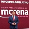 Diputado Iván Arévalo Vera hablando ante micrófonos y bandera de Michoacán durante presentación de informe legislativo en el Congreso estatal