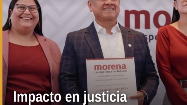 Carlos Torres Piña hablando ante militantes en Michoacán, con bandera de Morena y letrero que dice 'Defensa de la
