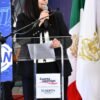 Teresita Herrera Maldonado hablando ante micrófonos en Morelia, con bandera de Michoacán al fondo, durante su Segundo