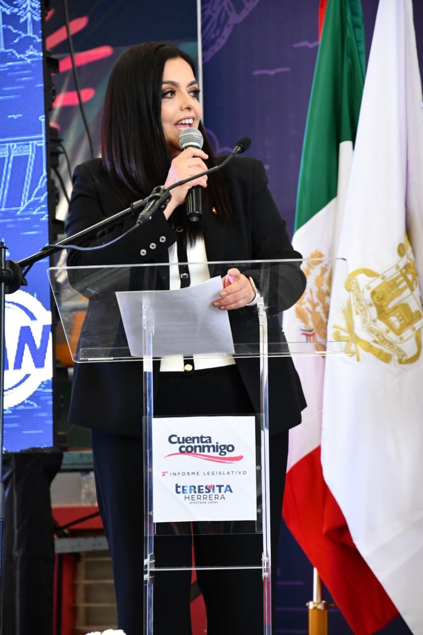 Teresita Herrera Maldonado hablando ante micrófonos en Morelia, con bandera de Michoacán al fondo, durante su Segundo
