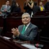 Diputado Juan Antonio Magaña de la Mora hablando ante micrófono en el Congreso del Estado de Michoacán, con bandera del