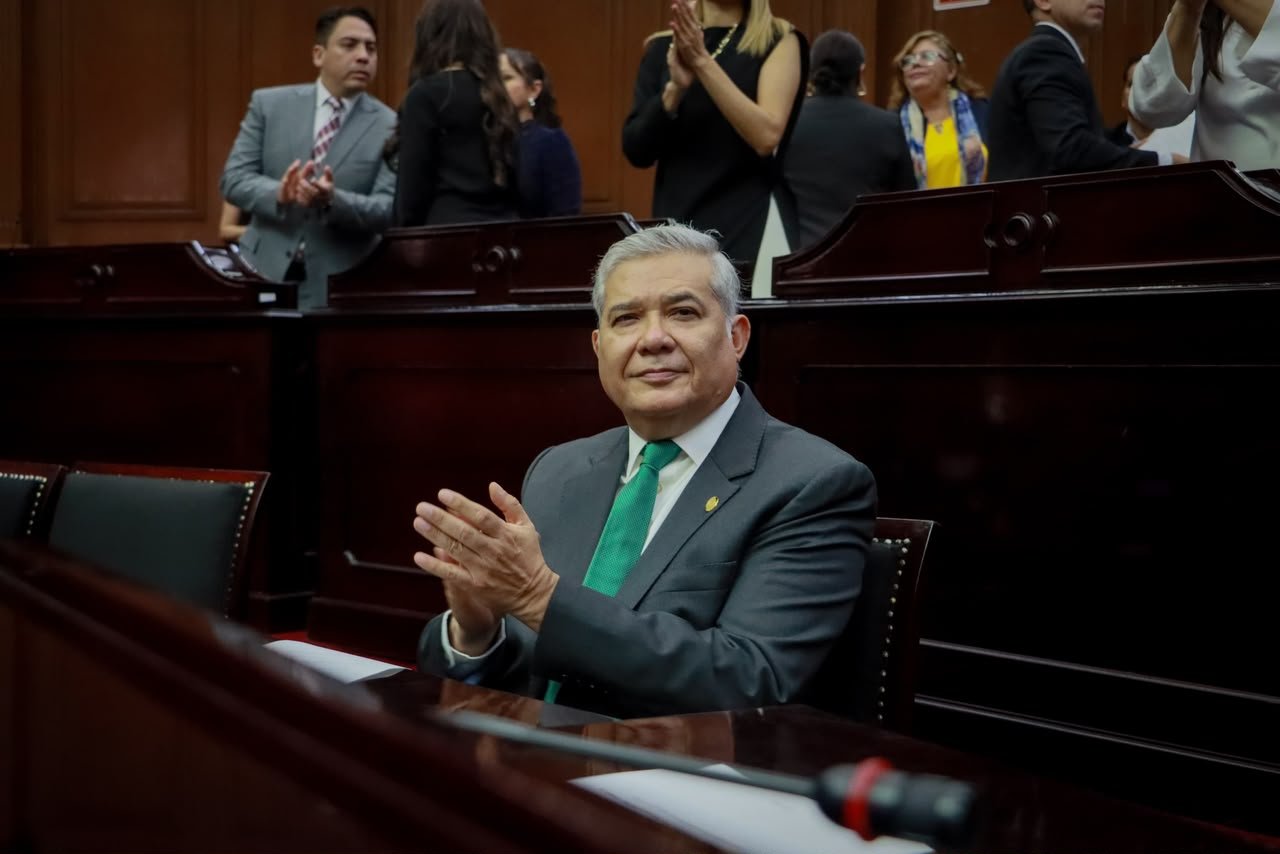 Diputado Juan Antonio Magaña de la Mora hablando ante micrófono en el Congreso del Estado de Michoacán, con bandera del