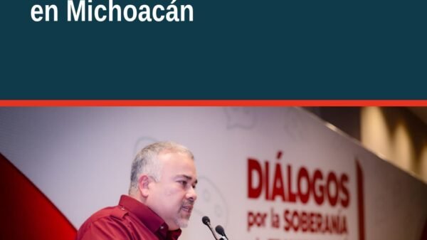 Carlos Torres Piña hablando frente a un grupo diverso de militantes de Morena en un evento en Morelia, con pancartas de la