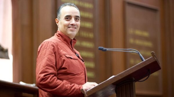 Fotografía de diputado Juan Pablo Celis Silva en sesión del Congreso del Estado en Morelia, con fondo de bandera mexicana y